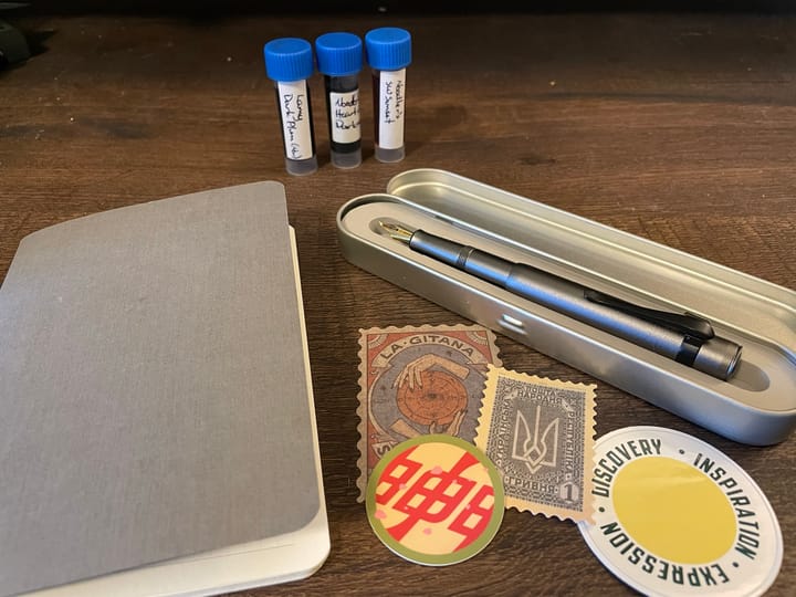 A grey notebook, stickers and a grey pen in a metal tin